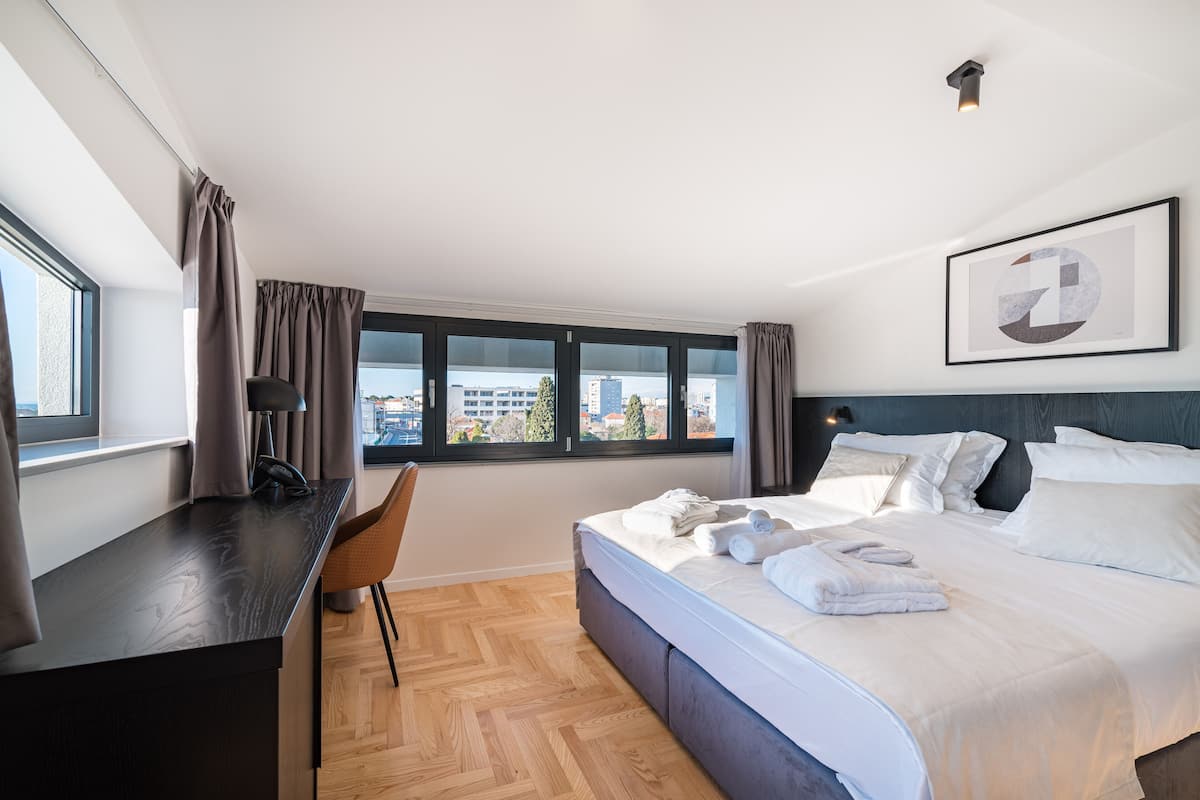 A modern hotel room with a large bed, a desk, and a view of the city.