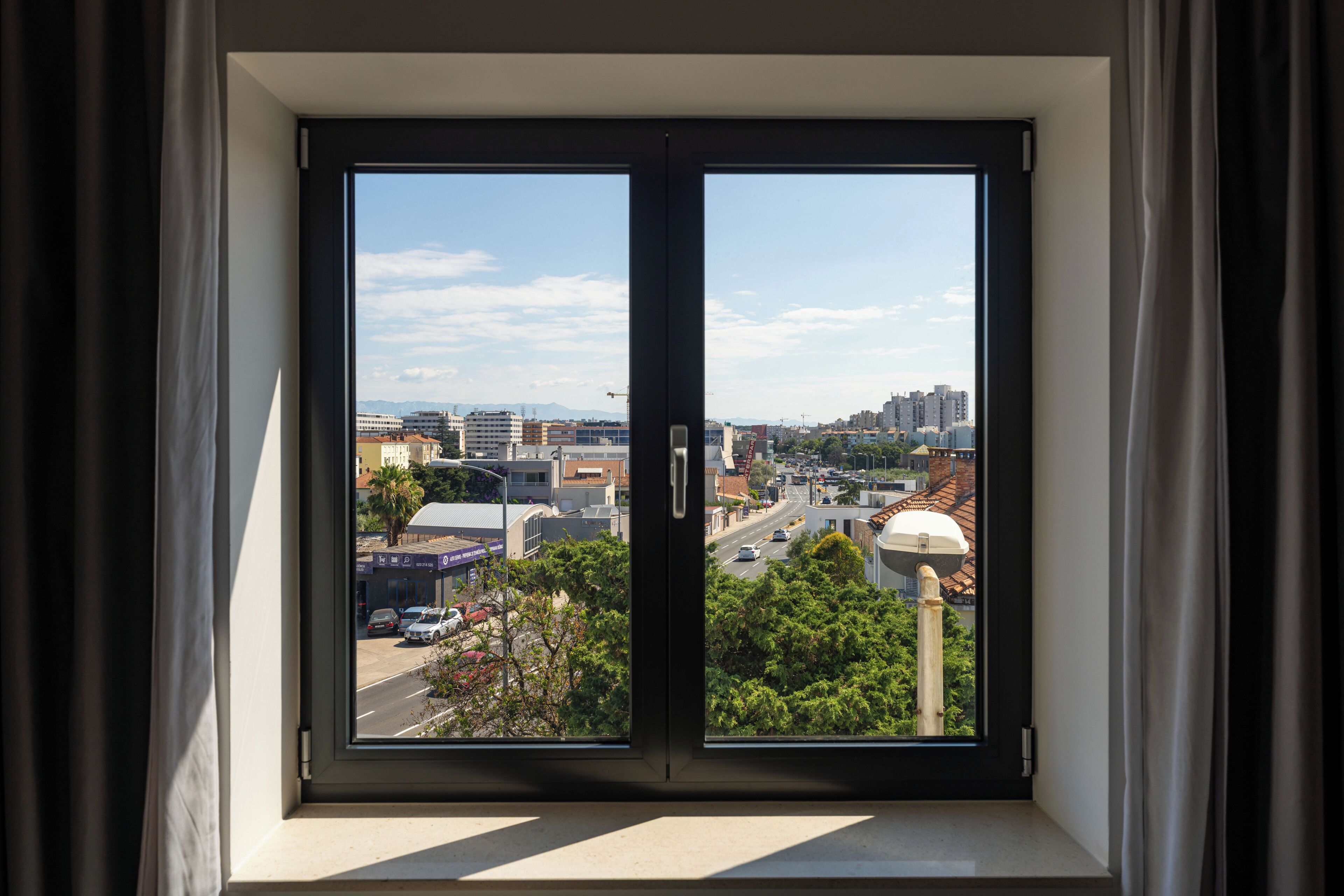 Vista a través de una ventana con cielo despejado, edificios y una carretera.