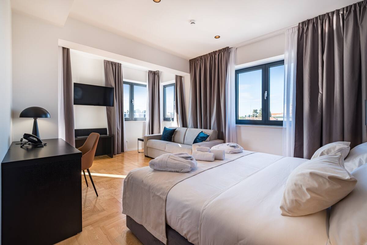 A modern hotel room with a large bed, a desk, a chair, and a flat-screen TV.