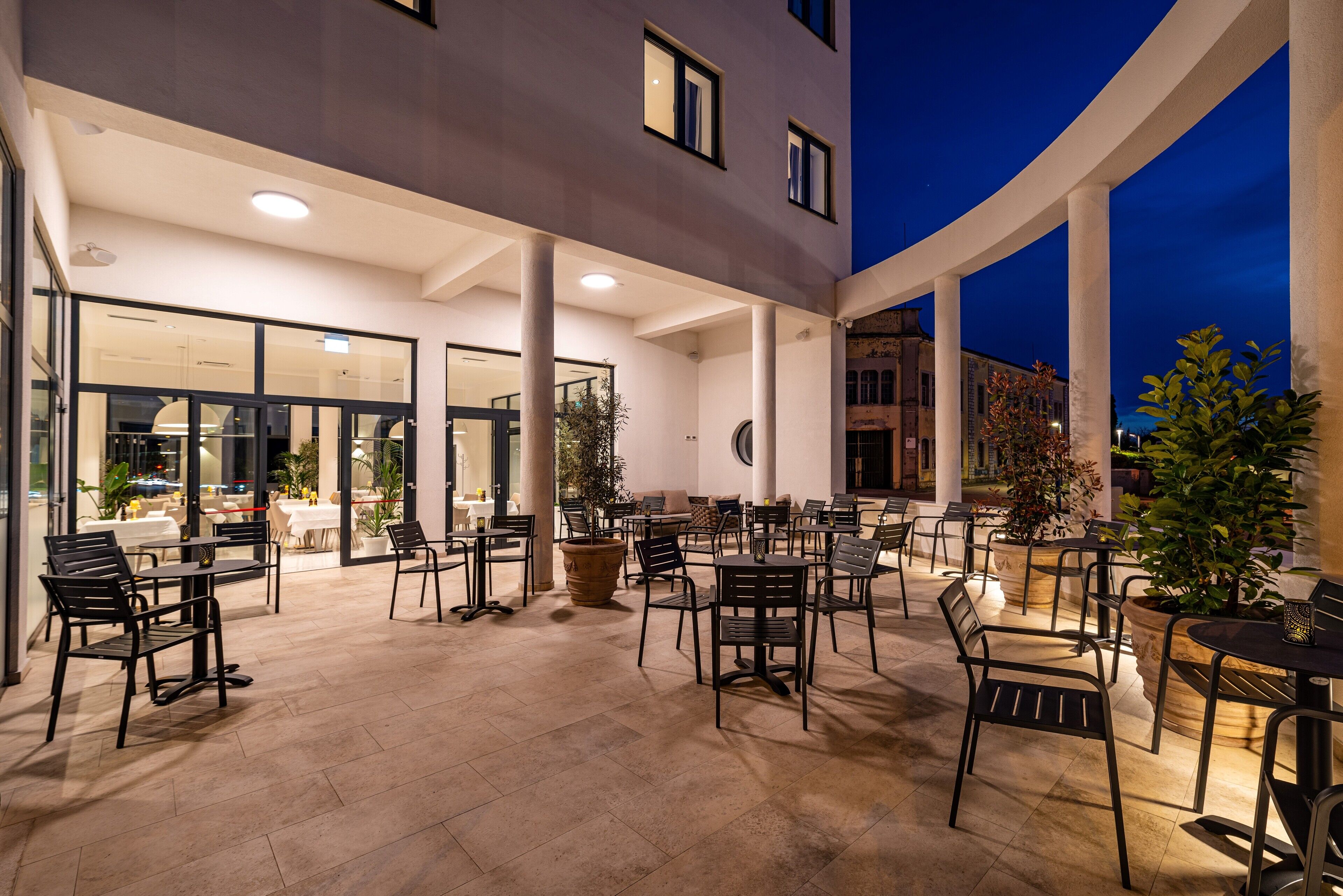 An outdoor patio area with tables and chairs, a building entrance, and potted plants.
