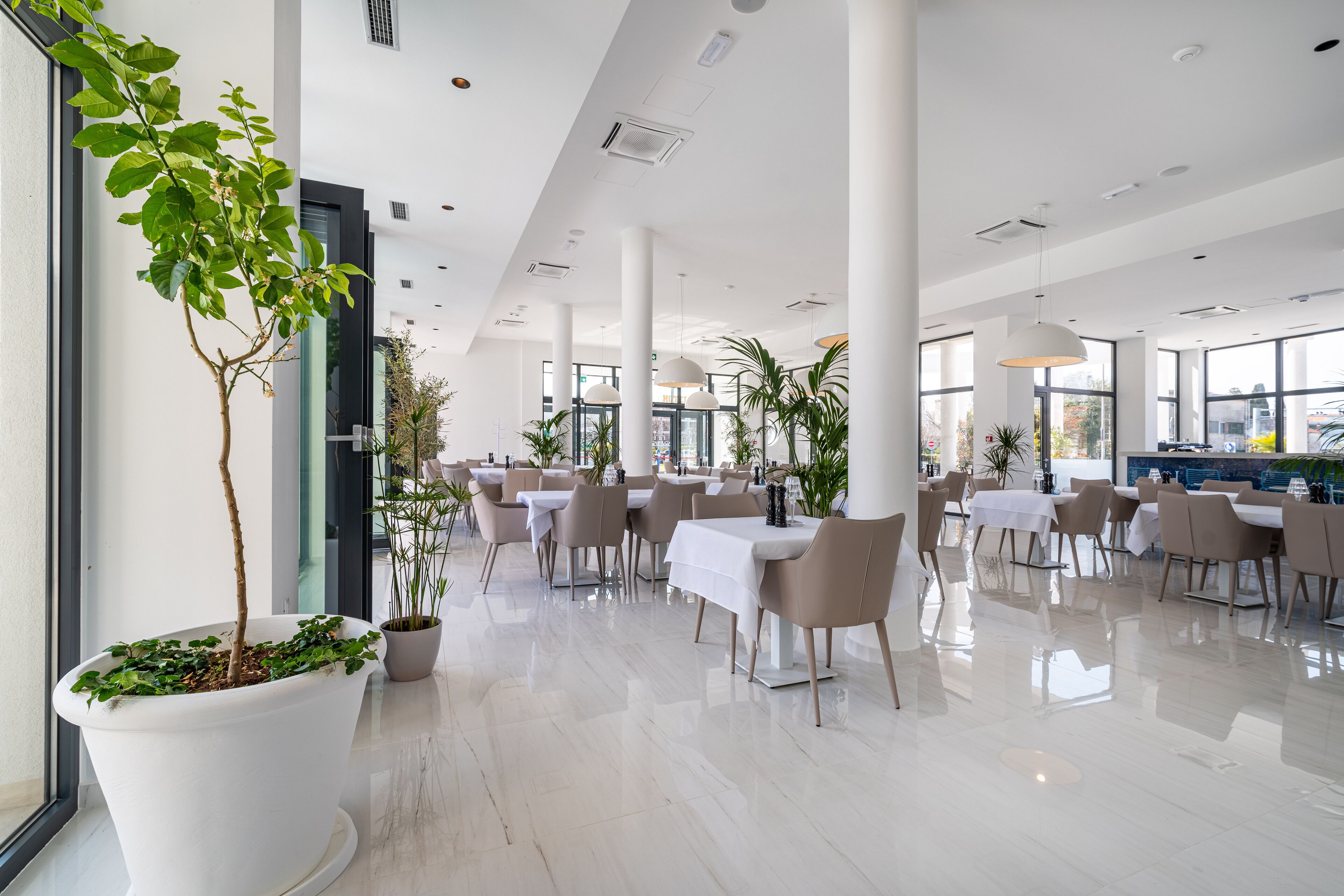 A spacious indoor dining area with high ceilings, large windows, and modern furniture.