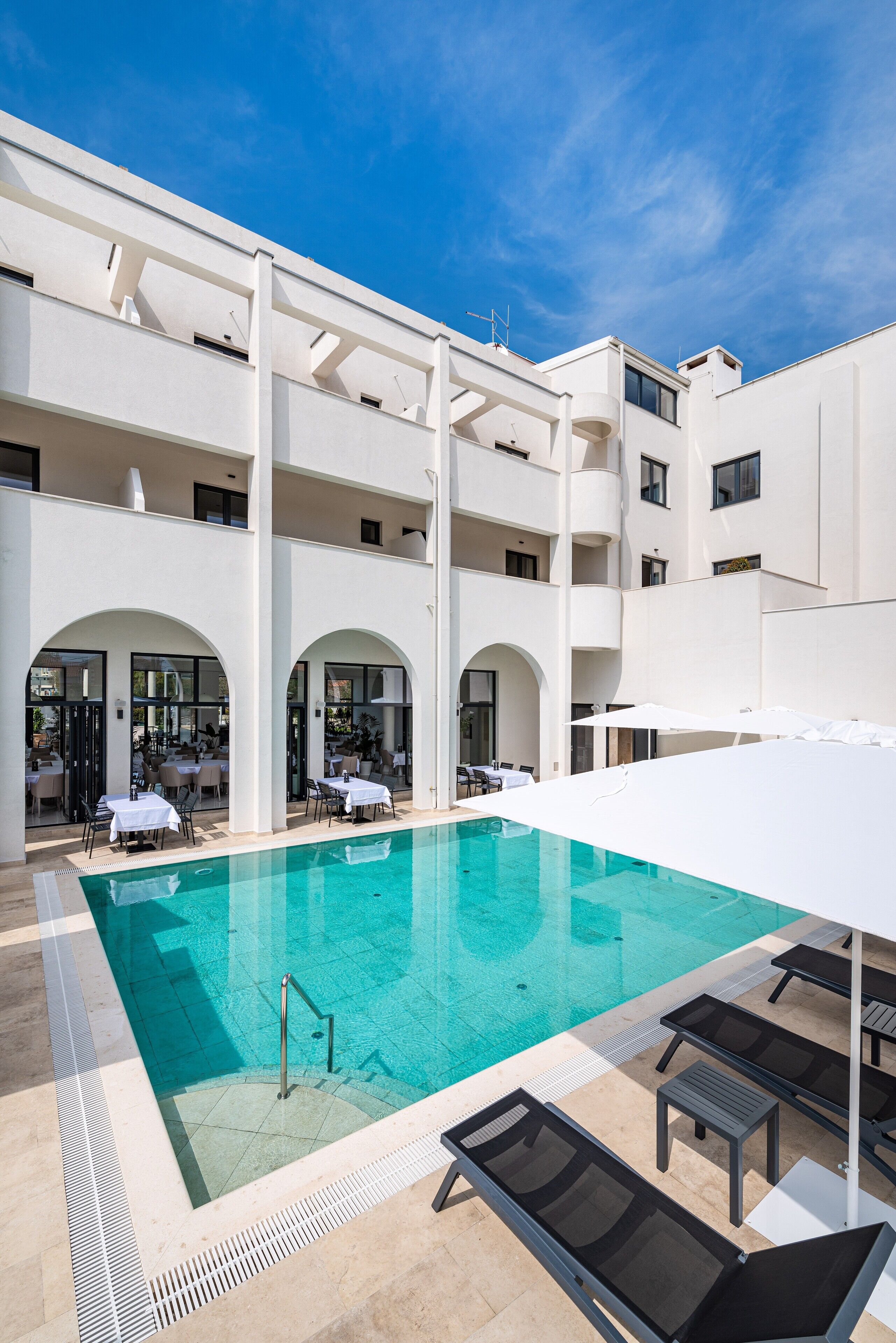 A modern hotel with a central swimming pool, outdoor seating, and a multi-level structure.