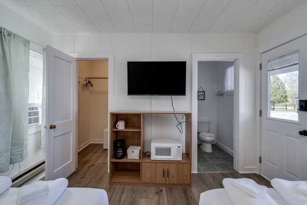 A hotel room with a wooden cabinet, a flat-screen TV, a white microwave, and a toilet visible through an open door.