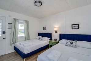 Une chambre avec deux lits, une fenêtre avec des rideaux, une lampe fixée au mur et des tableaux encadrés.