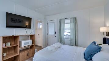 Une chambre d’hôtel avec un lit, un téléviseur fixé au mur, une étagère en bois et une fenêtre avec des rideaux.