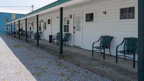 Une rangée de chambres de motel, chacune avec sa propre porte, un passage couvert et des sièges à l’extérieur.