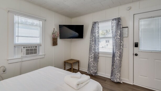 Ein Schlafzimmer mit einem Bett, einem Fernseher, einer Tür und Fenstern mit Jalousien.