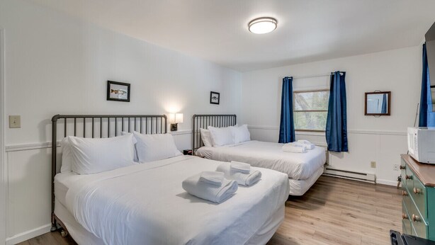 Ein Hotelzimmer mit zwei Betten, einem Schminktisch, einer Mikrowelle und einem Fenster mit Vorhängen.