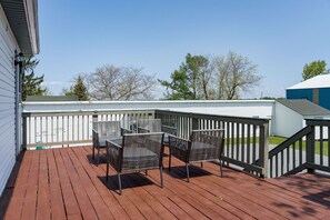 Eine Holzterrasse mit Metallstühlen und einem Geländer, mit Blick auf ein Gebäude und Bäume.