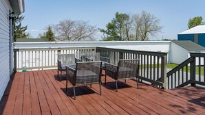 A wooden deck with metal chairs and a railing, overlooking a building and trees. - K's Motel with Stunning St. Lawrence River Views - Room 9 (Clayton)