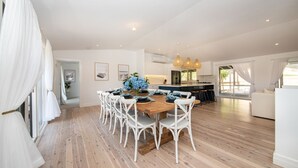 Un comedor amplio con mesa de madera y sillas blancas, una cocina con isla central y ventanas grandes que dejan entrar luz natural.
