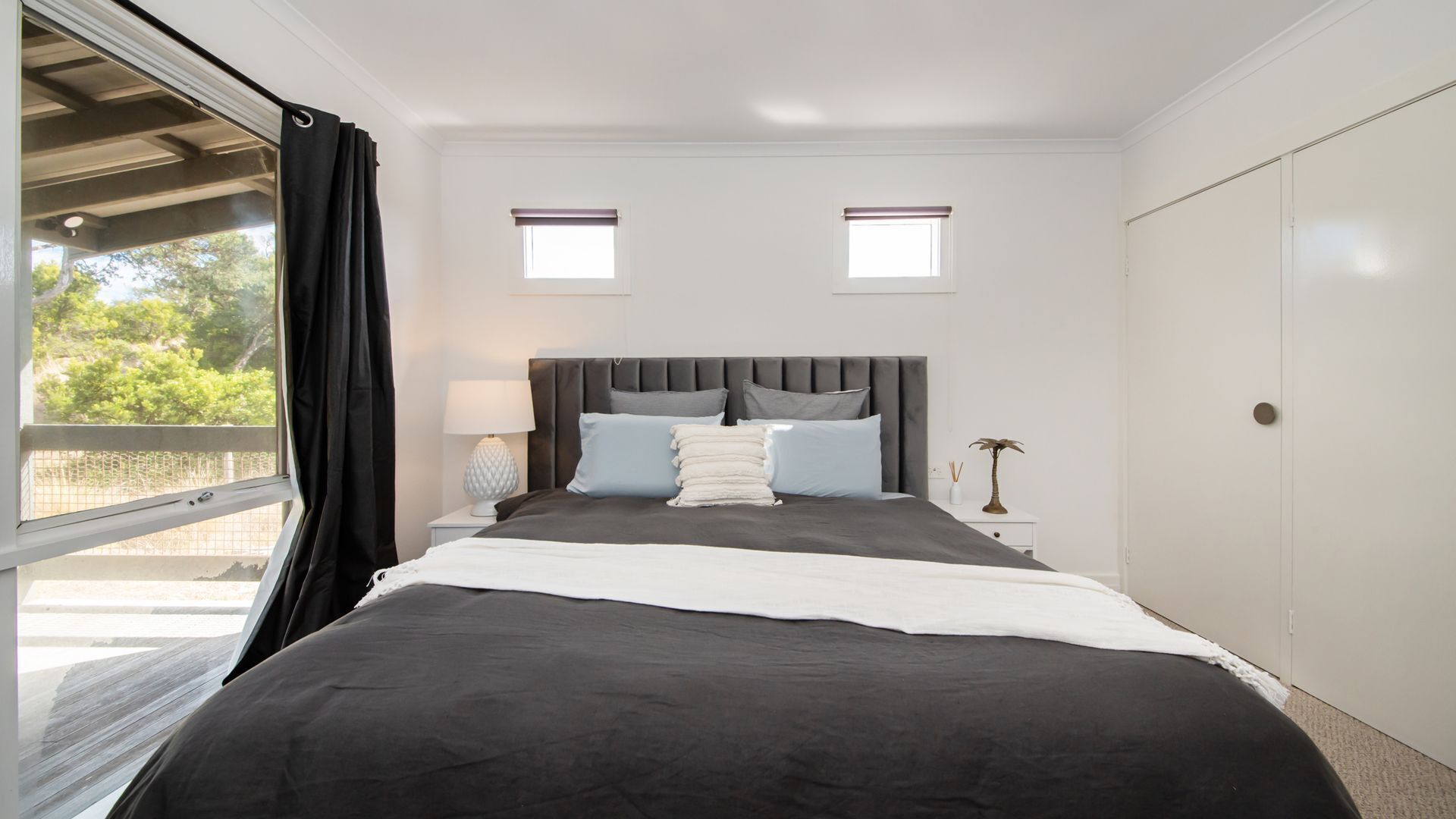 A bedroom with a large bed, two bedside tables, a nightstand, a window with curtains, and a door.