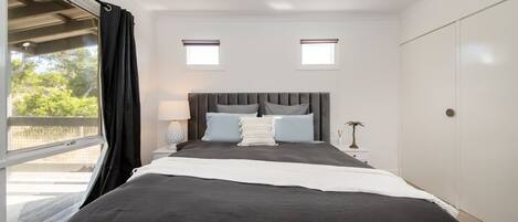 A bedroom with a large bed, two bedside tables, a nightstand, a window with curtains, and a door.