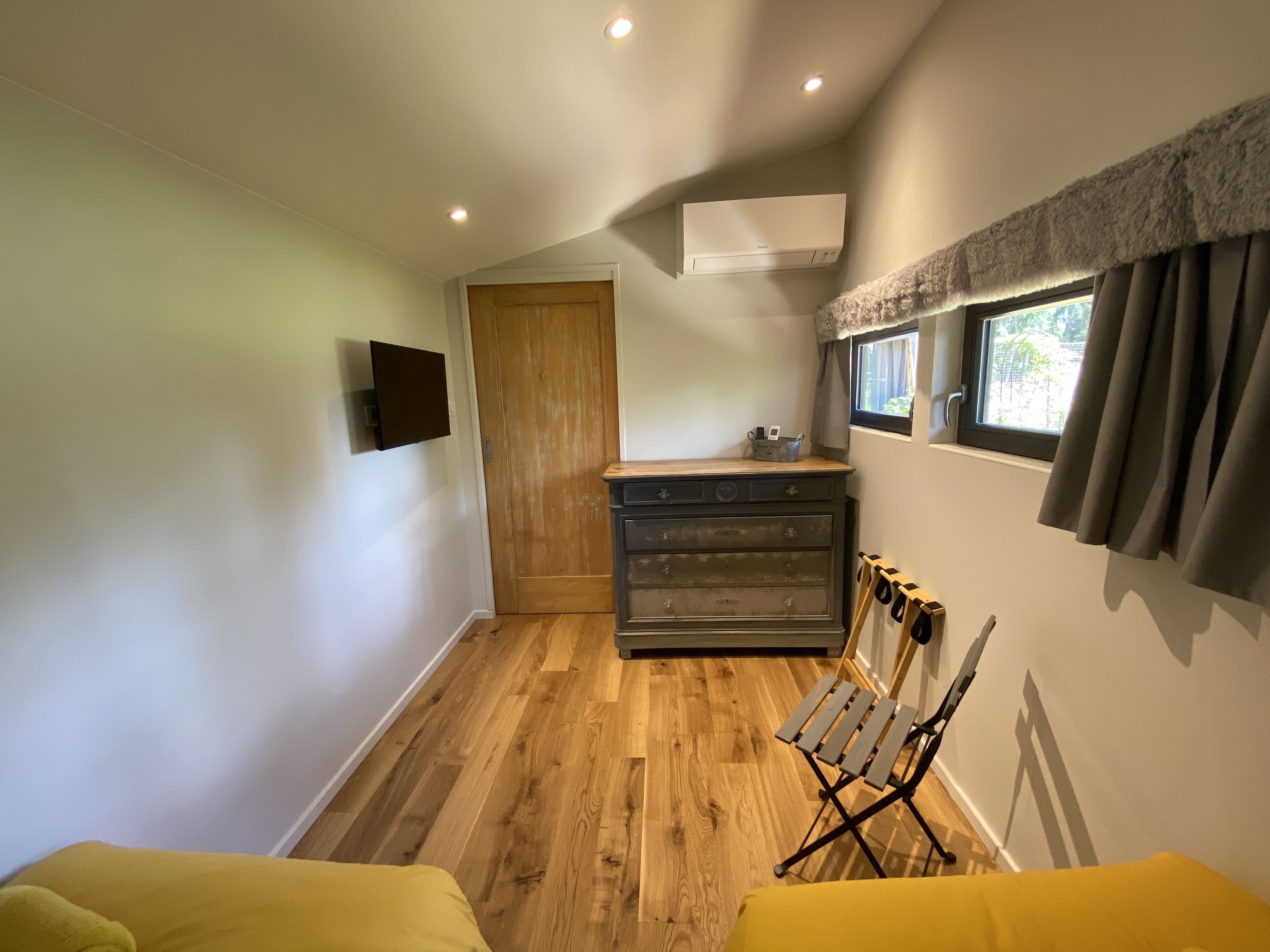 Une cuisine compacte avec un plancher en bois, un four encastré, une petite fenêtre avec des rideaux et un téléviseur fixé au mur.