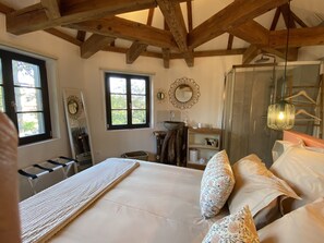 A bedroom with a large bed, a wooden ceiling, a window, a mirror, a bedside table, and a walk-in closet. - Le Parc du Séquoia : stay in a former apiary (Ostheim)