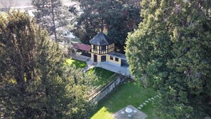 Una casa de dos pisos con torreta, rodeada de árboles frondosos.