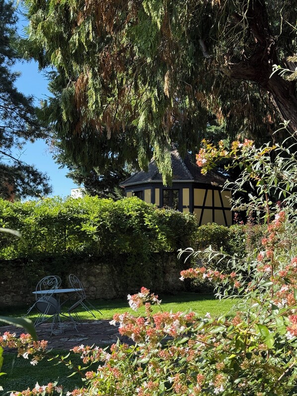 A traditional building with a dark roof and yellow trim, surrounded by lush greenery and flowering plants.