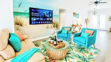 A living room with a beach-themed wall mural, two blue armchairs, a beige sofa, and a coffee table with drinks.
