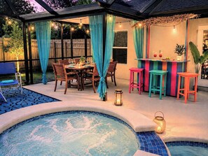A backyard with a pool, a dining table with chairs, a bar area, and a covered seating area.