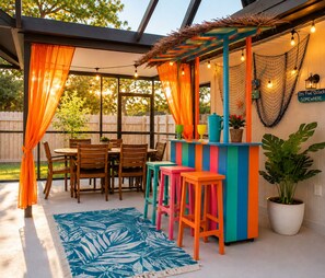Une terrasse extérieure avec une table et des chaises en bois, un coin bar aux couleurs vives et une plante en pot.