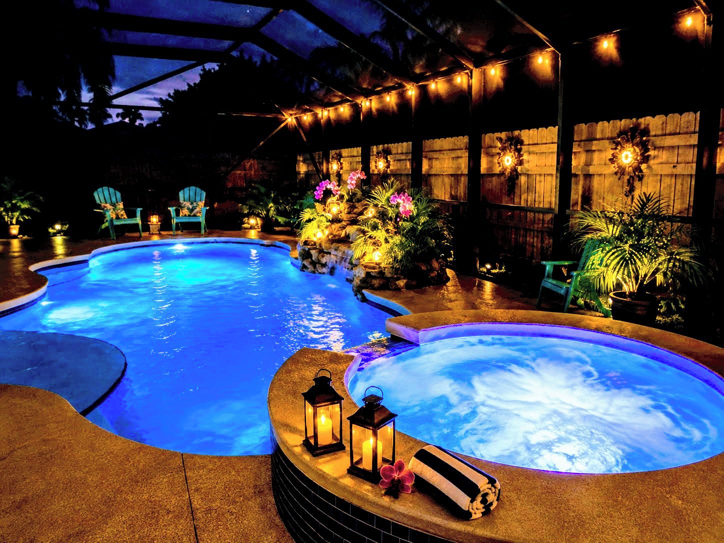 Una piscina con hidromasaje, rodeada de sillas y plantas en macetas, bajo una zona techada con luces colgantes.