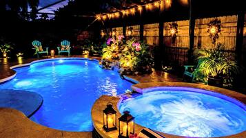 Una piscina con hidromasaje, rodeada de sillas y plantas en macetas, bajo una zona techada con luces colgantes.