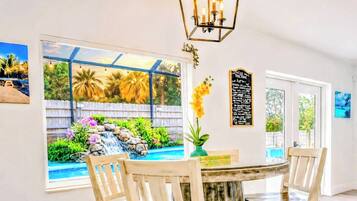 A dining area with a round table, four chairs, a view of a backyard with a pool and waterfall, and a chandelier.