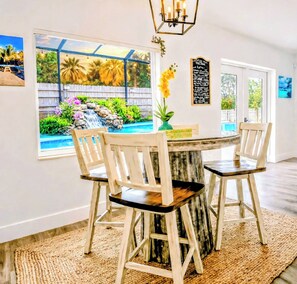 A dining area with a round table, four chairs, a view of a backyard with a pool and waterfall, and a chandelier.