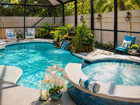 Piscina en un patio trasero con jacuzzi, rodeada de sillas y plantas en macetas.