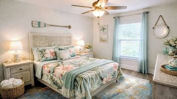 Un dormitorio con cama, mesitas de noche, ventilador de techo, ventana con cortinas y decoración en la pared.