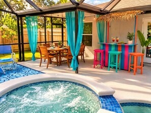 A backyard with a hot tub, a dining table with chairs, a bar area with stools, and a covered seating area.