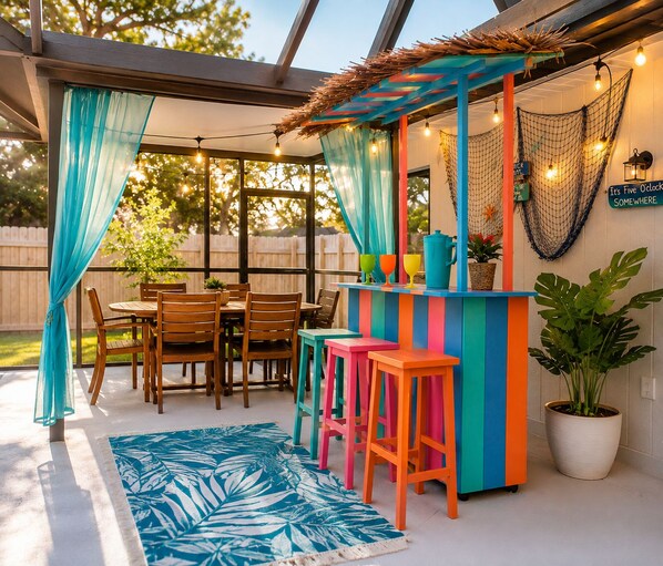 An outdoor patio with a wooden table and chairs, a colorful bar area, and a potted plant.