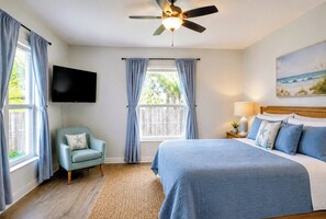 A bedroom with a bed, a television, a ceiling fan, and a window with curtains.
