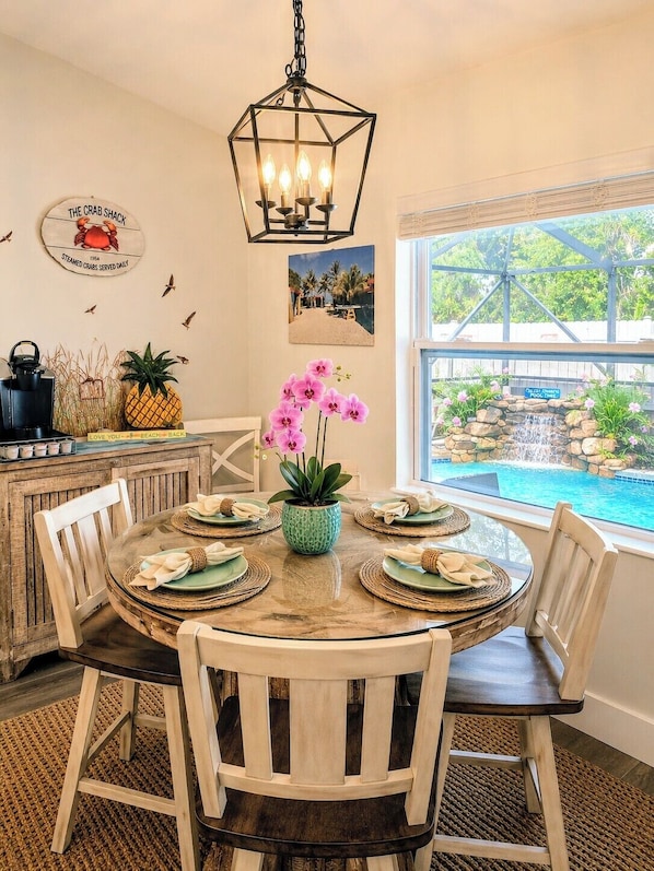 A dining area with a round table, chairs, and a view of a pool and waterfall.
