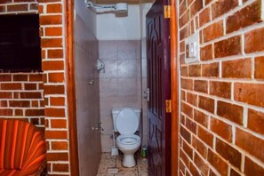 A narrow bathroom with a white toilet, a small trash bin, and a red chair. - Mufasa cottages (Nairobi)