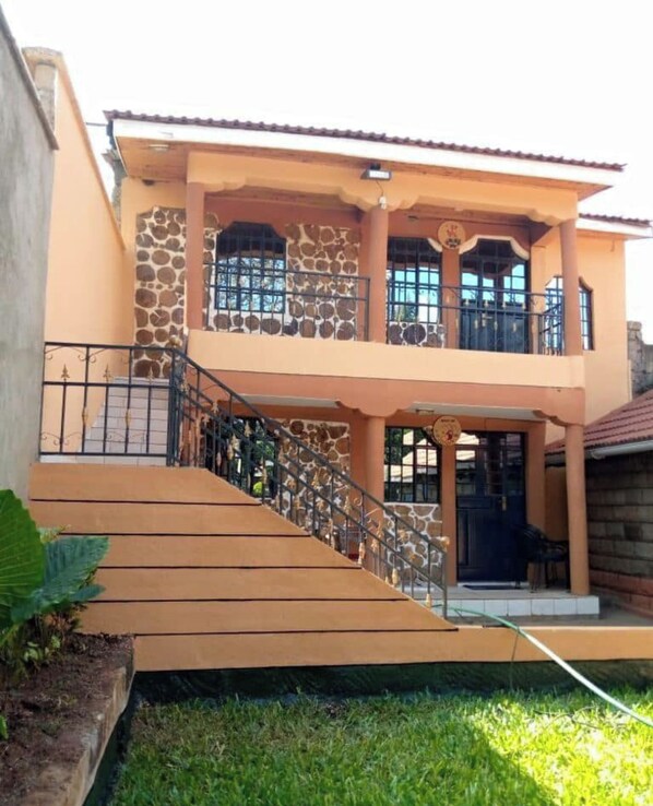 A two-story house with a stone facade, a balcony, and a staircase leading to the upper floor. - Mufasa cottages (Nairobi)