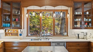 Una cocina con armarios de madera, un ventanal con vistas a árboles y lámparas colgantes.