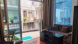 Un salón moderno con sofá, una mesa de centro y un sillón. Hay un balcón con plantas y vistas de la ciudad.