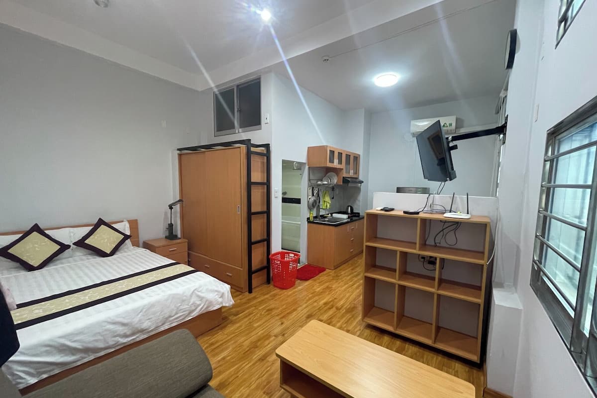 Ein gemütlicher Raum mit Bett, einer kleinen Küchenzeile, einem an der Wand montierten Fernseher und einem Fenster.