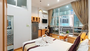 Habitación de hotel con cama, escritorio, silla, sofá, televisor y un ventanal con cortinas.