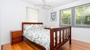 A bedroom with a wooden bed, a nightstand, a ceiling fan, and a window with blinds.