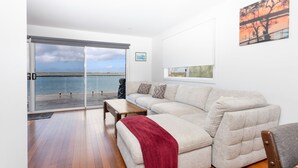 A living room with a sofa, a coffee table, and a view of the sea through a sliding glass door. - Omaroo - Absolute waterfront location (ILUKA)