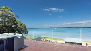 A deck with outdoor seating overlooking a calm body of water, a clear sky, and distant land. - Omaroo - Absolute waterfront location (ILUKA)