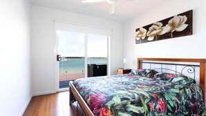A bedroom with a bed, a nightstand, a painting, and a view of the water through a sliding door. - Omaroo - Absolute waterfront location (ILUKA)