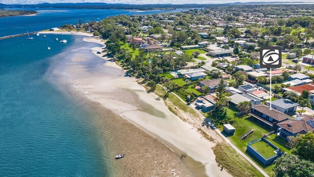 An aerial view of a coastal residential area with houses, a beach, and boats. - Omaroo - Absolute waterfront location (ILUKA)