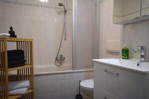 A bathroom with a bathtub, toilet, and a wooden shelf with towels.