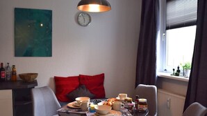 Un coin repas avec une table mise pour le petit-déjeuner, une horloge au mur et une fenêtre avec des rideaux.