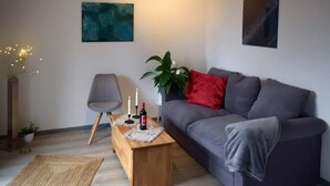 Un salon moderne avec un canapé gris, une table basse en bois ornée de bougies, un fauteuil gris et des tableaux abstraits accrochés aux murs.