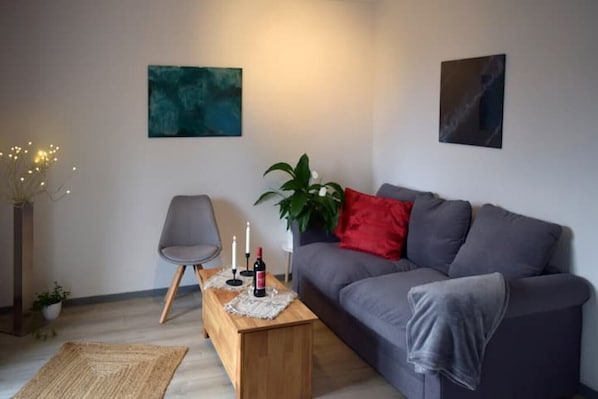 Un salon moderne avec un canapé gris, une table basse en bois ornée de bougies, un fauteuil gris et des tableaux abstraits accrochés aux murs.