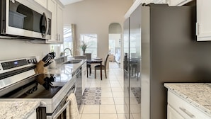 A modern kitchen with white cabinetry, stainless steel appliances, and a granite countertop. - Glenbrook Vacation Pool/Spa Home Near Disney (Clermont)